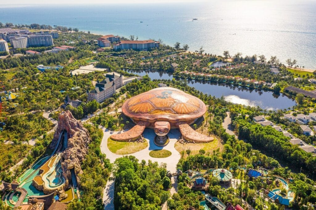 VinWonders Phú Quốc nhìn từ trên cao: toà thủy cung mái hình con rùa giữa vườn cây, công viên nước bên trái, biển Bãi Dài phía xa