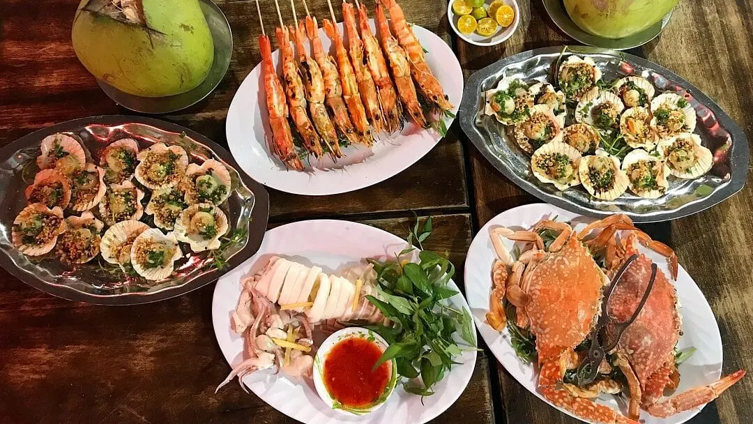 Mâm ghẹ, tôm nướng và sò điệp nướng mỡ hành trên bàn gỗ