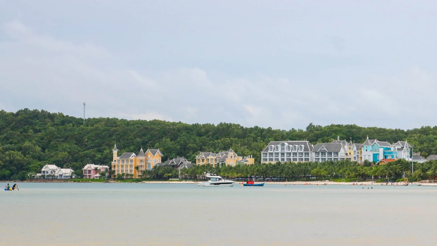Dãy resort nhiều màu sau hàng cây nhìn từ mặt biển, cano neo gần bờ