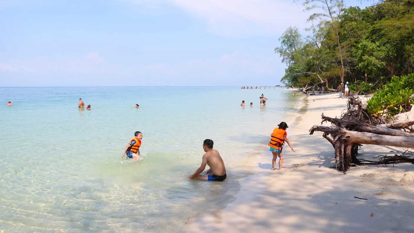 Trẻ em mặc áo phao cam chơi ở vùng nước nông cạnh bãi cát
