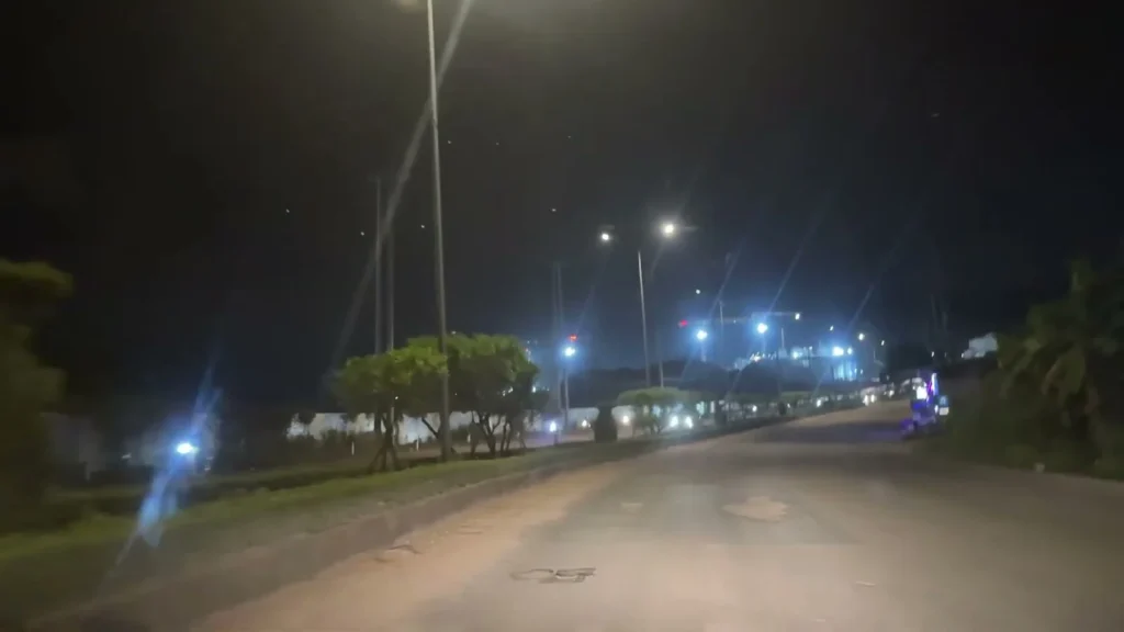 Đường rộng sáng đèn ban đêm, xa xa là công trình sáng đèn xanh trắng